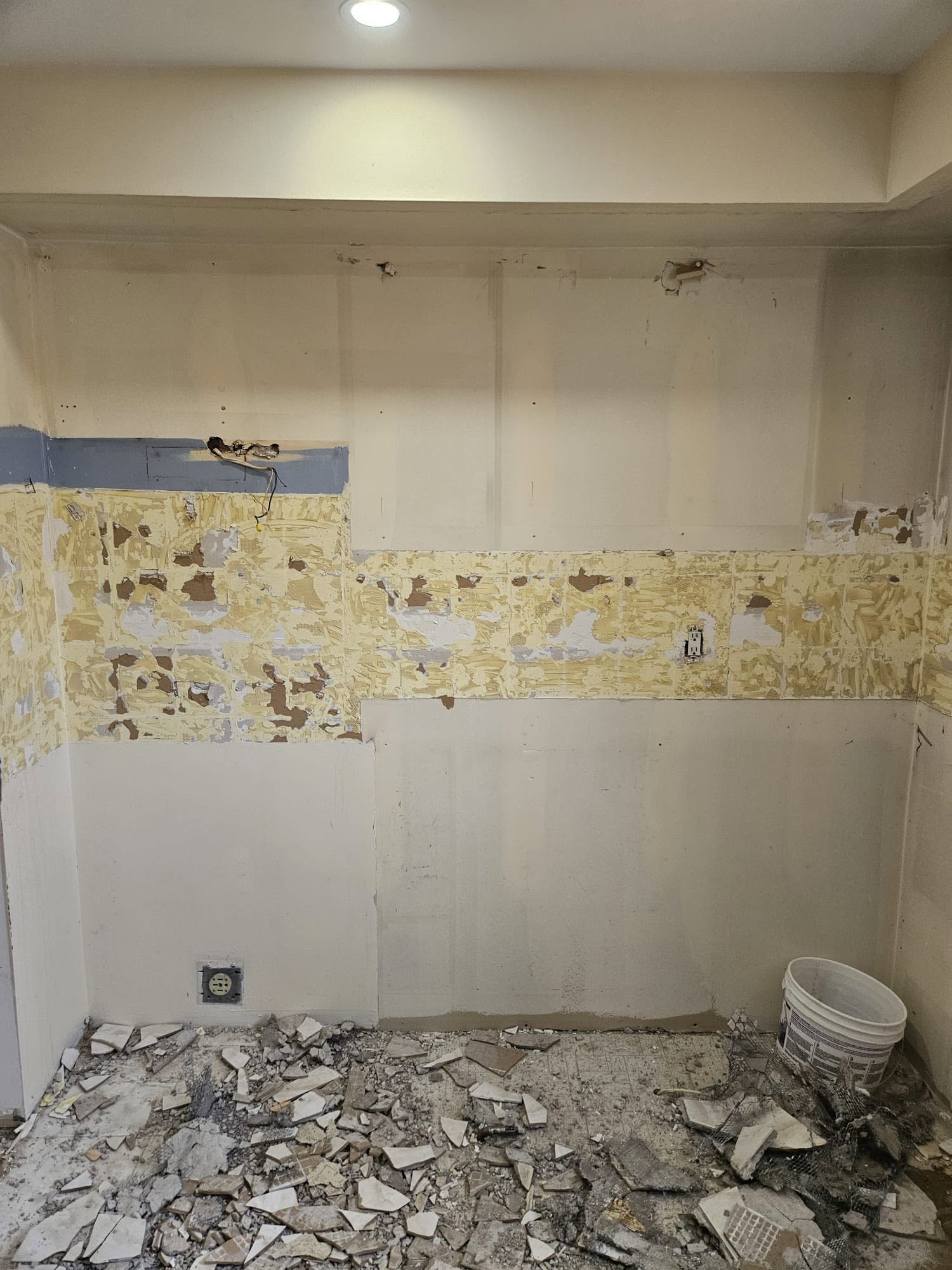 The kitchen wall before: cabinets removed, old tile adhesive on the walls, broken tile on the floor.